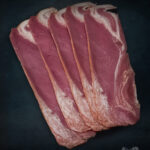 Beef Bacon Färse aus Pommern in frischen Scheiben auf dunklem Brett