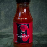 Glasflasche Eckart Ketchup No. 2 neben Bourbon-Whiskey-Flasche und Ahornsirup – Premium-Tomatenketchup mit edler Note.