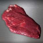 Flanksteak Simmentaler Alpenrind roh – zart marmoriertes Alpenweidefleisch auf gebürstetem Metall, elegant ausgeleuchtet