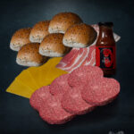Burger Bundle mit Färse-Patties, Bacon, Buns, Käse, Pfeffer und Sauce auf dunklem Untergrund arrangiert