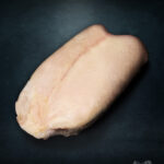 Roh geschnittene Gänsebrust aus Pommern in Extra-Qualität, feine Fleischstruktur, edel ausgeleuchtet vor metallischem Hintergrund