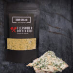 Schüssel mit Sour Cream Onion Dip, umgeben von Kräutern und Zwiebelstücken