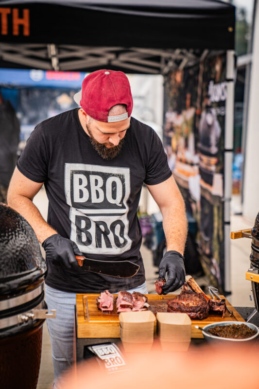 BBQbro André steht am Grill und bereitet BBQ Fleisch mit Rauch zu