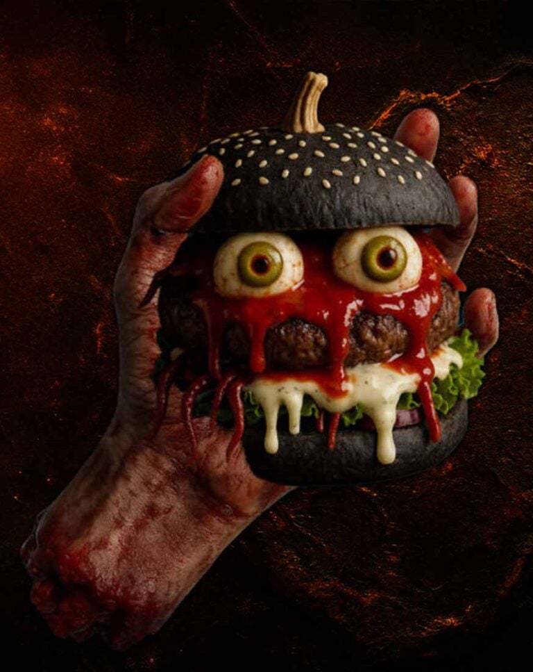 Halloween-Burger mit schwarzem Bun, weißen Sesamkörnern, essbaren Augen, roter Sauce, Käse und Salat, der von einer gruseligen Hand gehalten wird.