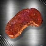 Rumpsteak vom Black Angus, kräftig mit Smoky-Pepper-Gewürz veredelt, auf einer metallischen Oberfläche präsentiert.