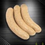 Feine Wildbratwurst aus regionaler Jagt: drei helle, gebogene Bratwürste mit kleinen dunklen Sprenkeln auf schwarzem Hintergrund.