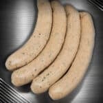 Vier Wildweisswürste aus deutschem Wildfleisch mit sichtbarer Petersilie auf dunklem Hintergrund.